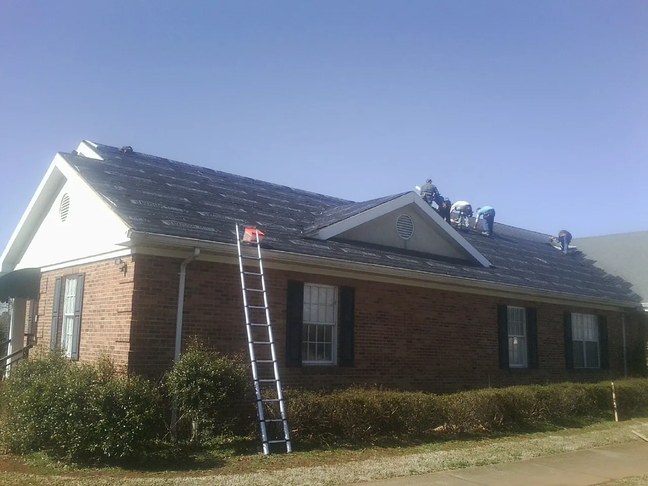 Crew tearing shingles off a brick ranch roof with a ladder set — Emergency Roof Repair work by our crew in Flossmoor