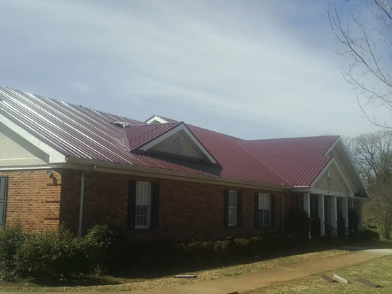 Red metal roof with gabled entries on a long brick building, from a Hail Damage Roof Repair job in Flossmoor