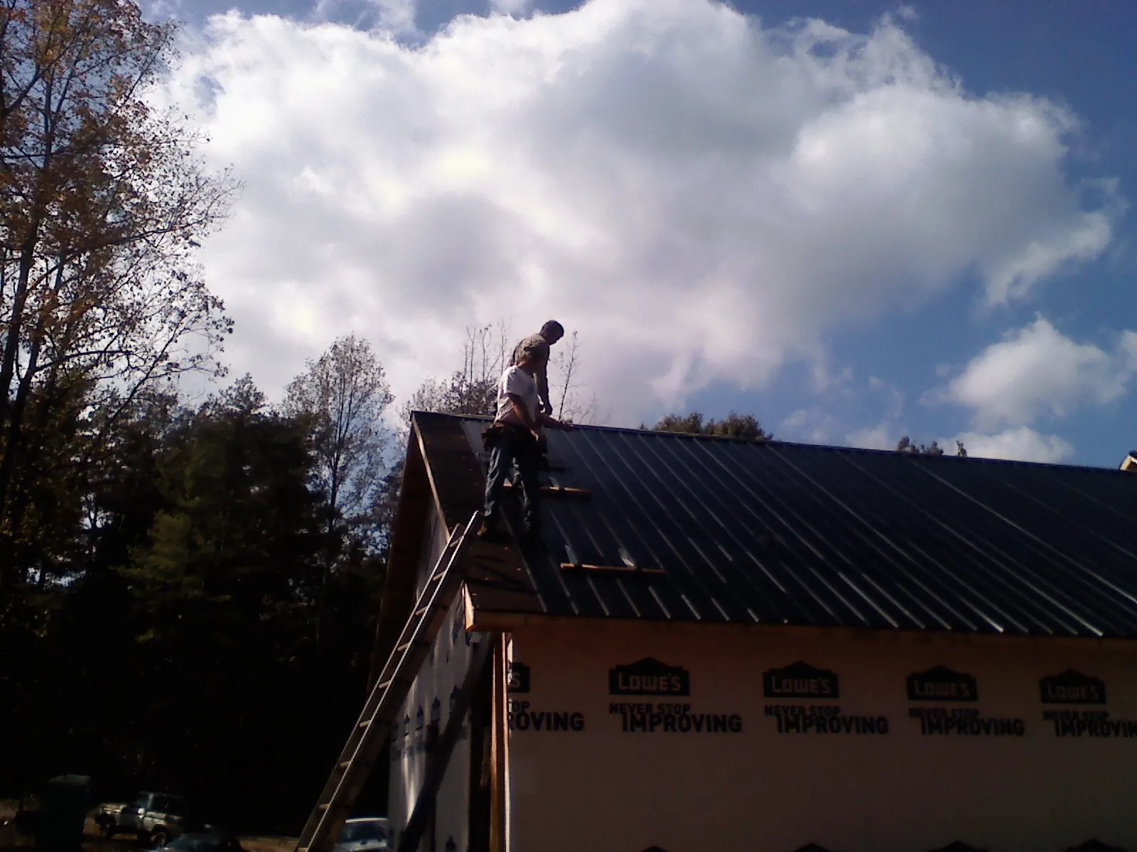 Roofer fastening dark metal panels high against a cloudy sky, from a Roof Inspection job in Flossmoor