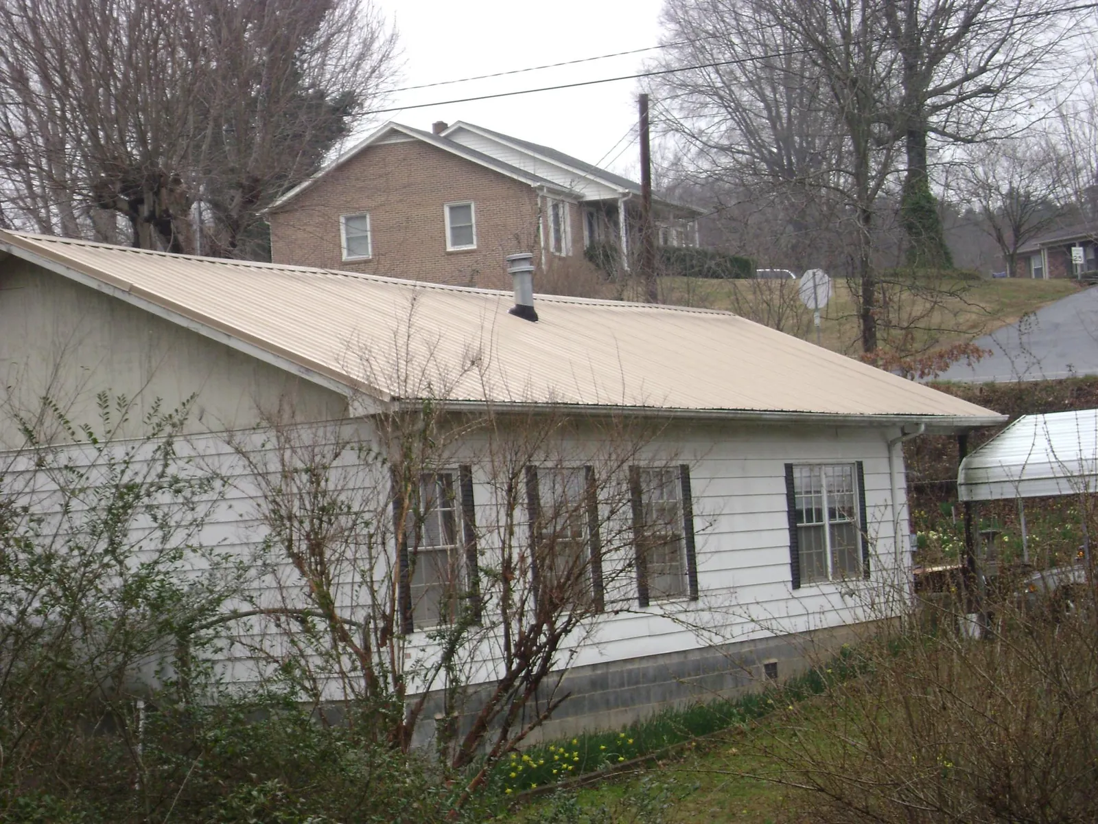 Tan metal roof on a white sided house set into a hillside — Commercial Roofing by Roofing Brothers in Flossmoor